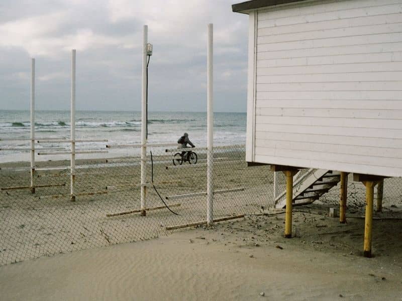 Surveyor measuring the elevation of a renovated beach house on pilings with an open lower level and raised mechanical equipment.